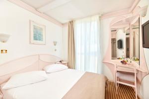 a white bedroom with a bed and a mirror at Hotel Zorna Plava Laguna in Poreč