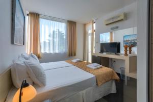a bedroom with a bed with a desk and a television at Hotel Odyssey Sozopol in Sozopol
