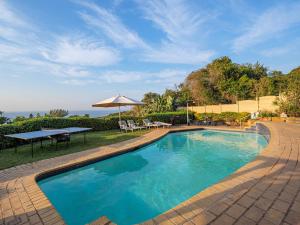 a swimming pool with a table and an umbrella at Umhlanga Beach House in Durban