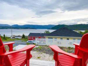 two red chairs sitting on a porch overlooking the water at The Rooms at Woody Point in Bonne Bay