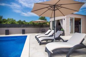 grupa krzeseł i parasol obok basenu w obiekcie Holiday home in Becici 35609 w mieście VeliGolji