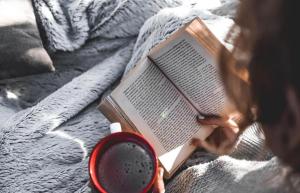 a person laying on a bed reading a book with a cup of coffee at Masinga in Hillcrest