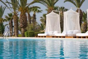 a pool with white chairs and palm trees at Sandy Beach Hotel & Spa - ex Sentido in Larnaca