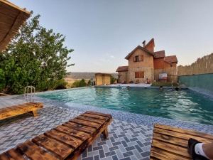 a swimming pool with two wooden benches in front of a house at Ferme D’hôte La Vallée in Azrou