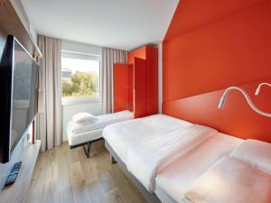 - 2 lits dans une chambre avec un mur orange dans l'établissement ibis budget Bayreuth, à Bayreuth
