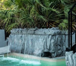 einem Wasserfall in einem Pool mit Palmen im Hintergrund in der Unterkunft Kiani Akti in Porto Rafti