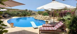 a swimming pool with two chairs and an umbrella at Dar Ta' Xmun - idyllic farmhouse with pool, garden, seaview & sunset in San Lawrenz