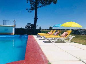 three lounge chairs with an umbrella next to a swimming pool at Monte Ramos in Ferreira do Alentejo
