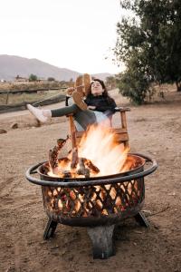 a woman sitting on a fire hydrant in the middle of a field at Lago Valle Wine Glamping in Valle de Guadalupe
