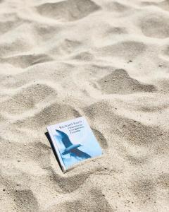 a book sitting in the sand on a beach at Poilsio namai Žuvėdra in Nida
