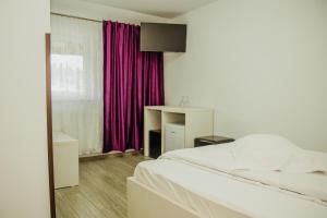 a bedroom with a white bed and purple curtains at Pensiunea Auras in Dorna Arini