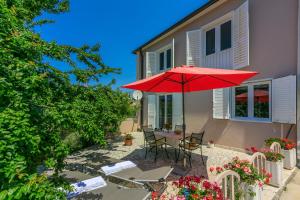 eine Terrasse mit einem Tisch und einem roten Regenschirm in der Unterkunft House Milenka in Banjol