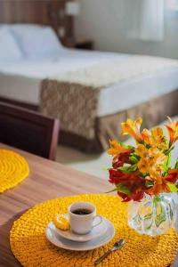 a table with a cup of coffee and a vase of flowers at Flat Completo para uma estadia perfeita NOTA FISCAL in Campos dos Goytacazes