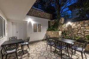 een patio met 2 tafels en stoelen en een stenen muur bij Cvrk Family House Novi Vinodolski in Novi Vinodolski
