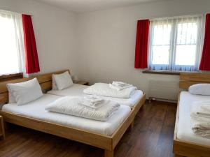 2 Betten in einem Zimmer mit Fenstern und roten Vorhängen in der Unterkunft Berggasthaus Piz Calmot in Andermatt