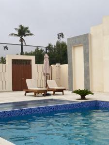 a swimming pool with two lounge chairs and an umbrella at Hawana Salalah lagoon beach apartment in Salalah