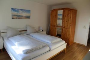 ein weißes Bett in einem Zimmer mit einem Holzschrank in der Unterkunft Ferienwohnung Strandblick, Ferienanlage "Blaumuschel" in Lubmin