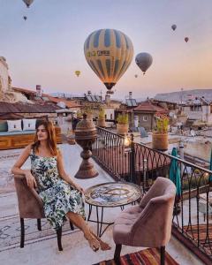 a woman sitting on a balcony with hot air balloons at Caftan Cave Suites in Göreme