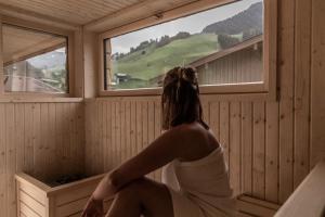 a woman sitting in a sauna looking out the window at FRAU GANS - pure mountain apartments in Saalbach-Hinterglemm