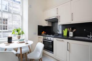 a kitchen with white cabinets and a white table and chairs at Stockbridge Two Bedroom Apartment in Edinburgh