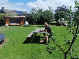 a woman sitting on a picnic table in a yard at Shelter Slotsgaarden in Jels