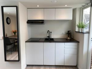 a kitchen with white cabinets and a sink and a mirror at Cozy Tiny House Egmond aan Zee- 500m from Beach-North Sea in Egmond aan Zee