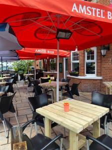 un patio con mesas y sillas con sombrillas rojas en The Emmbrook Inn Hotel, en Wokingham