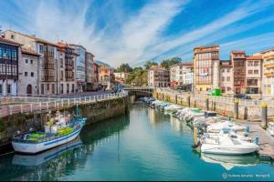 een groep boten aangemeerd in een rivier met gebouwen bij Adosado La Concha in Llanes