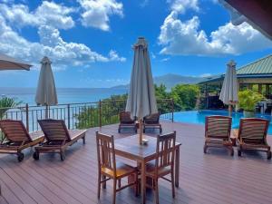 eine Holzterrasse mit Stühlen, einem Tisch und Sonnenschirmen in der Unterkunft Treasure Cove Hotel & Restaurant in Bel Ombre