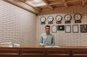 un hombre sentado en un escritorio con relojes en la pared en Hotel Dilshoda, en Samarkand