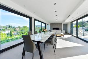 - une salle à manger avec une table, des chaises et de grandes fenêtres dans l'établissement SERRENDY - Custom villa with swimming pool, à Mandelieu-la-Napoule