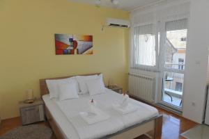 a bedroom with a bed with white sheets and a window at Angellina Apartmani in Sremska Mitrovica