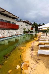 a swimming pool next to a building with white chairs at ILE DE PIPA LUXO in Pipa