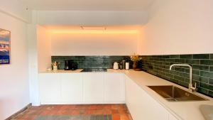 a kitchen with white cabinets and green tiles on the wall at House C in De Haan