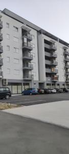 a large white building with cars parked in a parking lot at Apartman Mateja in Trebinje