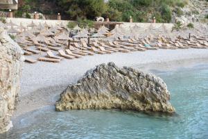 a group of lounge chairs and a large rock on a beach at Inn Hotel in Vlorë