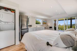 a white bedroom with a large bed and a kitchen at Sea-esta Suite with Ocean Views in Brentwood Bay in Brentwood Bay