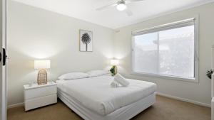 a white bedroom with a bed and a window at Sea For Miles - Scenic Coastal Retreat in Lakes Entrance