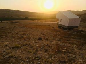 een klein huisje in een veld met de zonsondergang op de achtergrond bij פטריוט -יקב ננה in Mitzpe Ramon