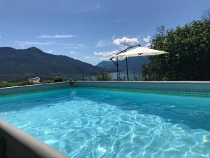 a swimming pool with an umbrella and mountains in the background at Agriturismo Ai Ronchi in Sorico