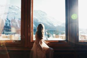 a woman in a wedding dress looking out of a window at Carlton Hotel St Moritz - The Leading Hotels of the World in St. Moritz