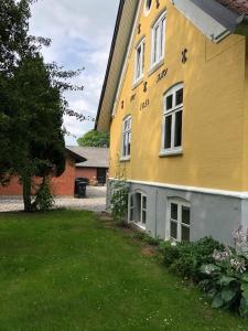 a yellow building with windows and a green yard at Allesø Gl. sognefoged gård in Odense