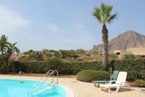 una piscina con due sedie e una palma di Casa Vacanze Libeccio - Villetta con giardino e piscina condominiale a Custonaci