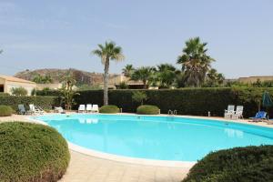 a large blue swimming pool with chairs and palm trees at Casa Vacanze Libeccio - Villetta con giardino e piscina condominiale in Custonaci