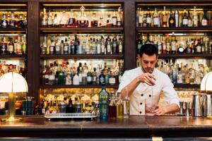 a man standing behind a bar holding a drink at Rosewood London in London