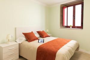 um quarto branco com uma cama grande com almofadas laranja em A Casa Antiga do Monte Apartamentos Turísticos - Lestrove em Padrón