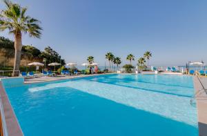 a large swimming pool with palm trees and the ocean at Monica Isabel Beach Club in Albufeira