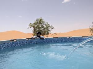 a man standing next to a swimming pool at Sahara Majestic Luxury Camp in Merzouga