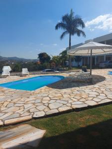 a swimming pool with an umbrella and a palm tree at Pousada Escarpas in Capitólio