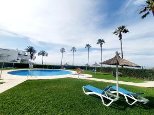 a pool with two chairs and an umbrella and palm trees at Marbellamar Seaviews in Cabopino